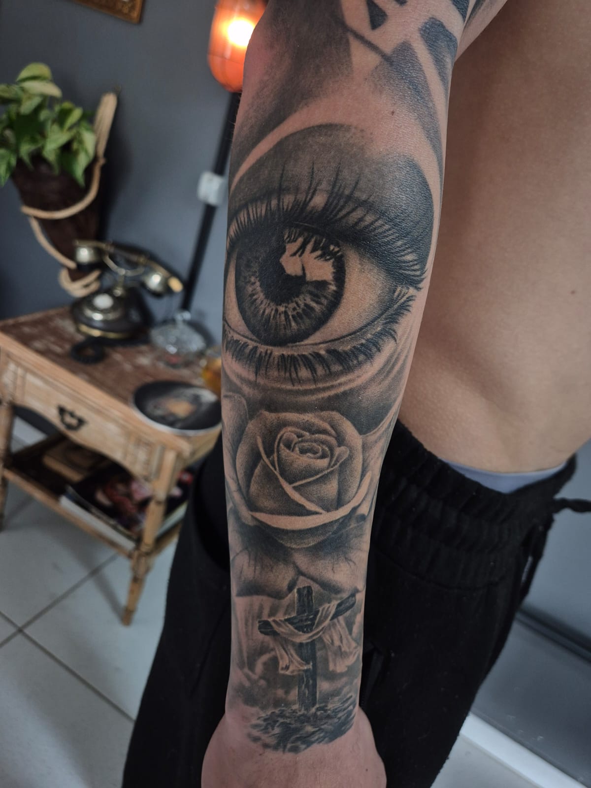 Tatuagem realista de olho, rosa e cruz no antebraço